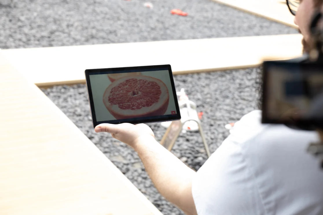 A person holding a reflective tablet display outdoors with a grapefruit on its screen
