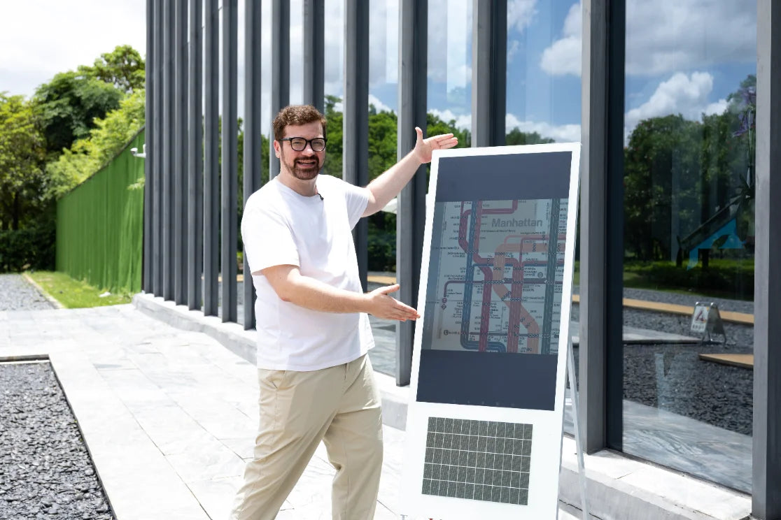 A presenter beside a reflective display panel showing a transit map outdoors in daylight